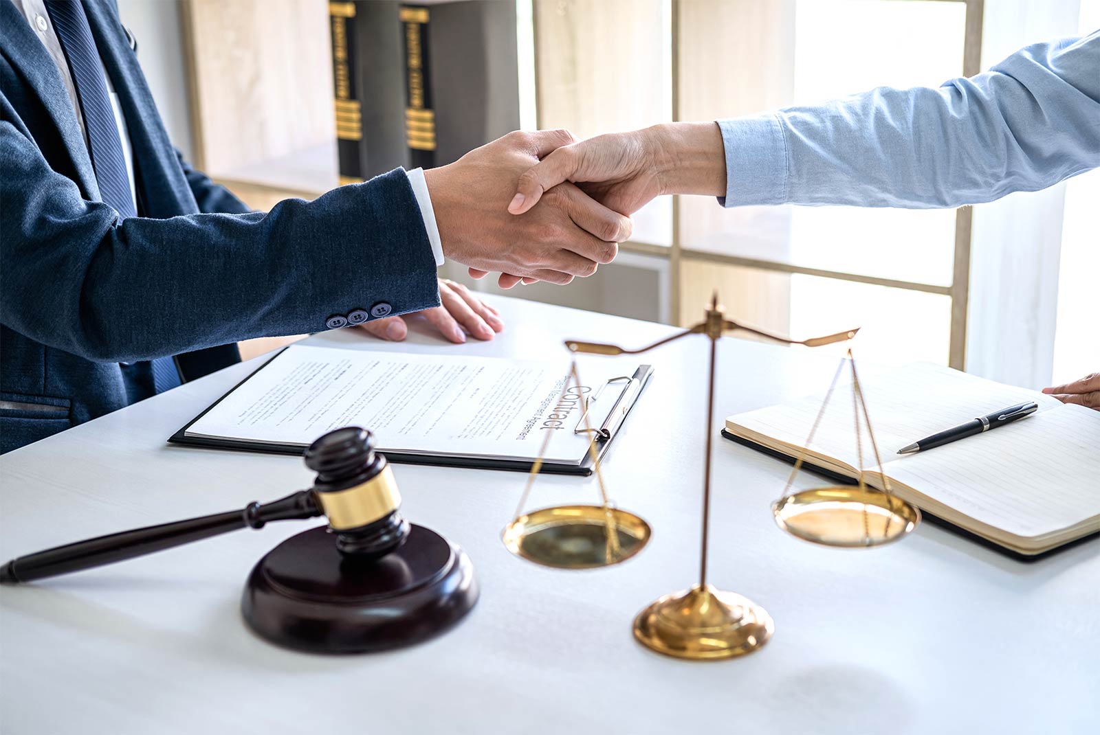 Fotografía de dos ejecutivos dándose la mano con un martillo y una balanza de justicia